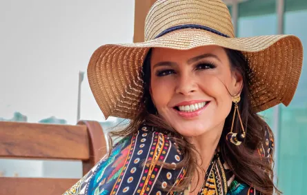 فتاة باسمة ترتدي قبعة من الخوص وتبتسم بسعادة وهي جالسة على مقعد خشبي