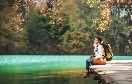 مسافرة تجلس على جسر خشبي على بحيرة جبلية في يوم خريفي مشمس