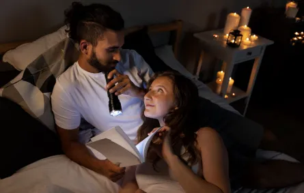 زوج يقرأ مع زوجته بعض الرسائل بالمساء على ضوء كاشف تجمعهما الرومانسية