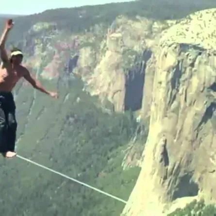 شاهد مغامراً يمشي على حبل مربوط بين جبلين