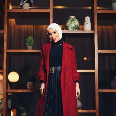 زهراء أشكناني بتنورة بليسيه طويلة ومعطف أحمر داكن مع إيشارب أبيض 