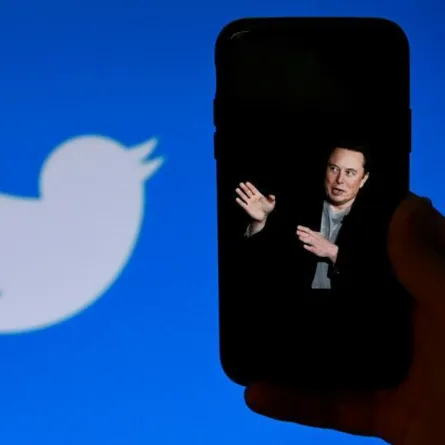 In this photo illustration, a phone screen displays a photo of Elon Musk with the Twitter logo shown in the background, on October 4, 2022, in Washington, DC. Elon Musk has offered to push through with his buyout of Twitter at the original agreed price, reports said Tuesday, prompting a surge in the share price of the social network that triggered a suspension of trading. OLIVIER DOULIERY / AFP