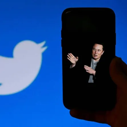 a photo of Elon Musk with the Twitter logo shown in the background, on October 4, 2022, in Washington, DC. Elon Musk has offered to push through with his buyout of Twitter at the original agreed price, reports said Tuesday, prompting a surge in the share price of the social network that triggered a suspension of trading. OLIVIER DOULIERY / AFP