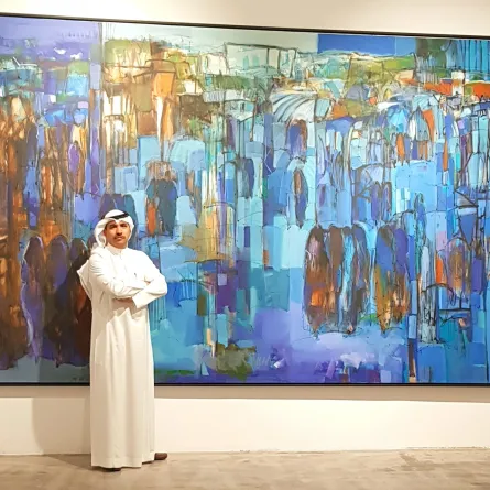 الفنان عبدالله الأحمري بجانب لوحته المعروضة في صالة آرت فيجن