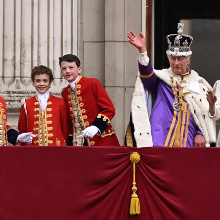 King Charles III wearing the Imperial state Crown, and Britain's Queen Camilla wearing a modified version of Queen Mary's Crown, flanked by Britain's Prince George of Wales (2nd L) and other pages of honour, wave from the Buckingham Palace balcony after viewing the Royal Air Force fly-past in central London on May 6, 2023, after their coronations. Oli SCARFF / AFP