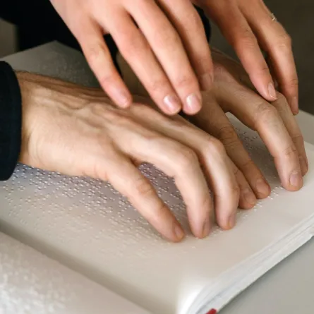 أصابع شخص يلمس شخص آخر يقرأ بطريقة برايل 