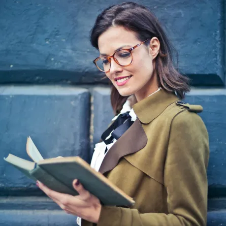 شابة ناجحة ترتدي نظارة تقرأ كتابًا تمسكه بيدها