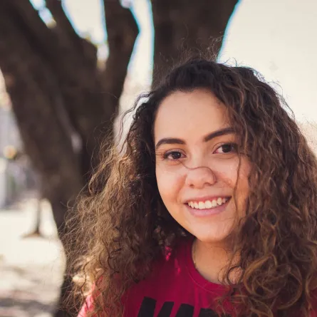 فتاة تبتسم في سعادة تقف ويبدو وراءها جذع شجرة