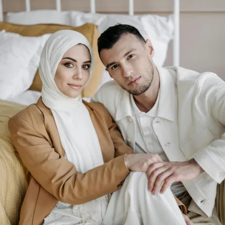 زوج يمسك يد زوجته وهما يجلسان على الأرض بجوار السرير بحجرة النوم ويبدوان سعيدين