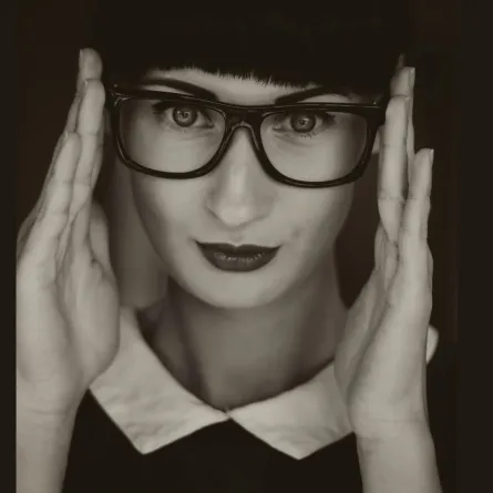 فتاة تبدو أمارات الذكاء على وجهها ترتدي نظارة وتثبتها بكلتا يديها على وجهها