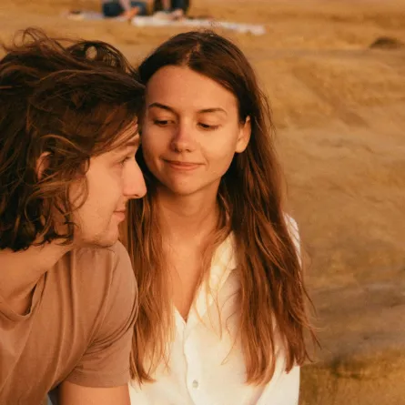 زوج محب صامت ينظر بهدوء بينما زوجته تتأمله بمحبة وهما جالسان بين أحضان الطبيعة