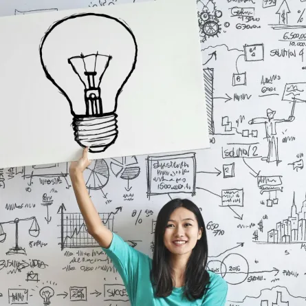 فتاة مخترعة تمسك بيدها لوحة مرسوم بها مصباح على سبورة بها مسائل حسابية كناية عن تفتح عقلها المخترع