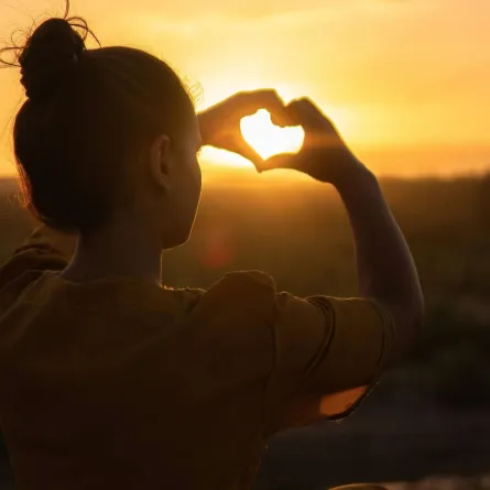 فتاة تصنع قلبًا تحتجز أشعة الشروق بكلتا يديها