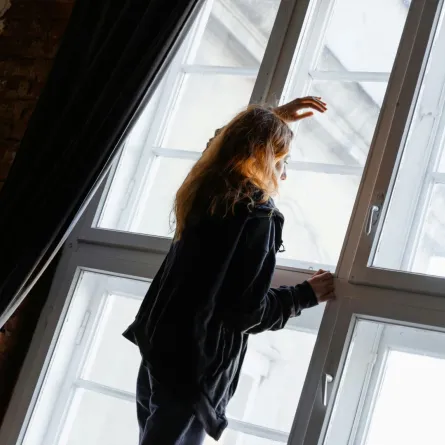 فتاة تستند برأسها بحزن على الشباك تطاردها الأفكار السلبية