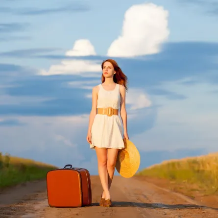 امرأة شابة جميلة تحمل قبعة وبجانبها حقيبة سفر