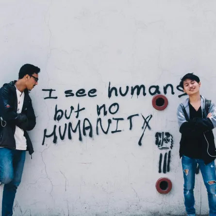شابان يقفان أمام كتابة على الحائط "أنا ارى إنسان ولكن لا أرى إنسانية"