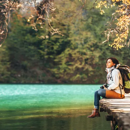 مسافرة تجلس على جسر خشبي على بحيرة جبلية في يوم خريفي مشمس