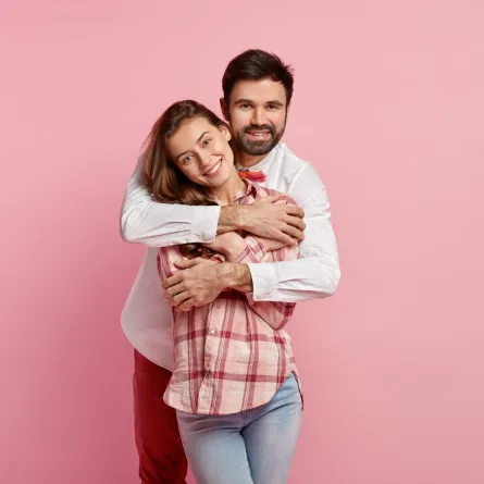 زوج يحتضن زوجته بحنان وهي تبتسم له بسعادة 