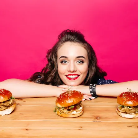 فتاة متكئة على طاولة خشبية مع ثلاثة برغر لذيذة 