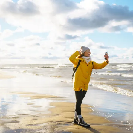 سائحة ترتدي سترة صفراء تلتقط صورة عند البحر وقت الغروب