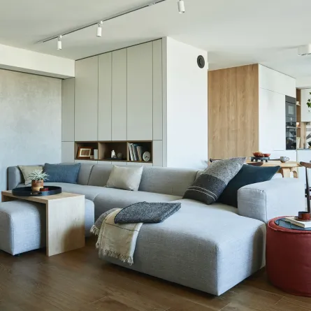 غرفة معيشة مع أريكة رمادية منخفضة ومطبخ في الخلفية