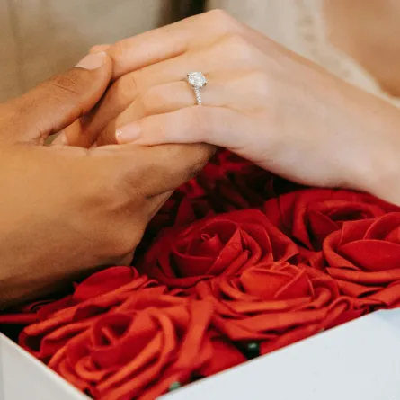 خطيب يمسك بيد خطيبته ويظهر خاتم الخطبة الماسي فوق باقة من الزهور الحمراء