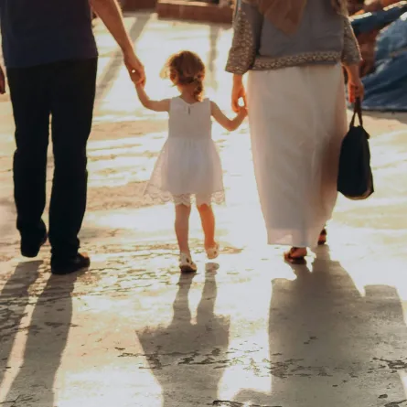 زوج وزوجه يمسكان بيد صغيرهما ويتنزهان في ضوء الشمس 