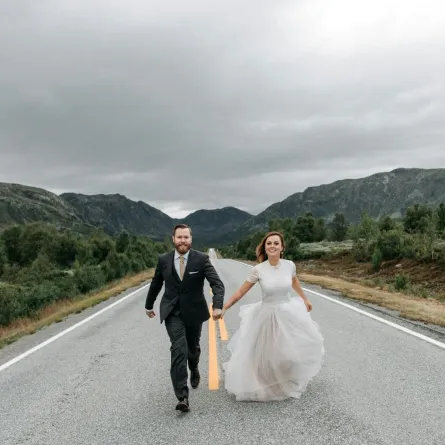 زوج يمسك بيد زوجته في زفافهما ويجري معها بسعادة