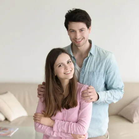 زوج يحتضن كتف زوجته ويبتسم بمحبة وهي تبتسم بسعادة   