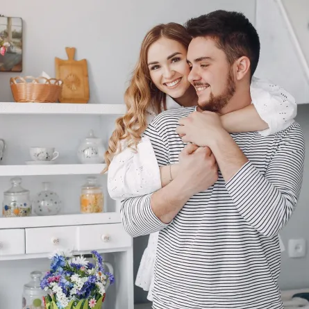 زوجة تحتضن ظهر زوجها وهو يمسك يديها وهما يبتسمان 