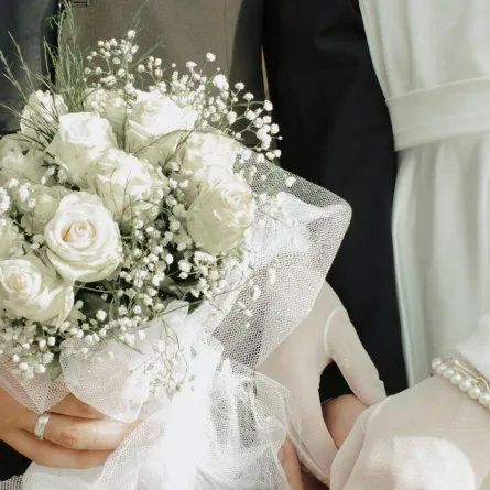زوج يمسك بيد زوجته في حفل الزفاف ويمسك بيده الأخرى باقة زهور الفرح