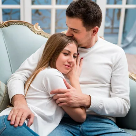 زوجة شابة تستلقي على صدر زوجها وهما جالسان على الأريكة 