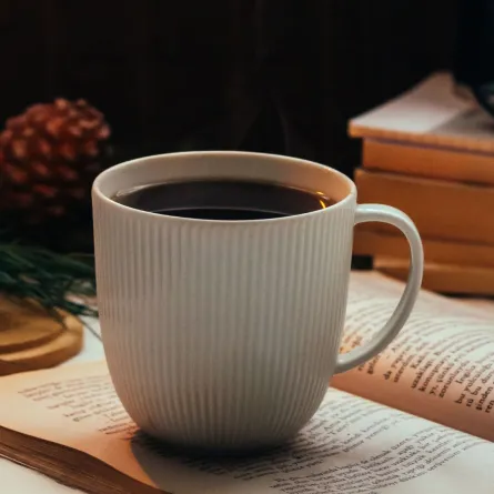 فنجان قهوة المساء فوق صفحات كتاب بجواره شمعة 
