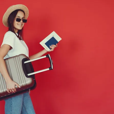 فتاة تحمل حقيبة أمتعتها وباسبورها وهي تبتسم بسعادة