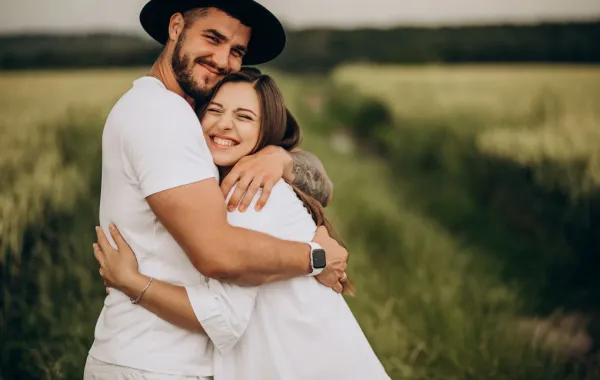 زوج يحتضن زوجته بحنان ومحبة وهي تبتسم بسعادة بين أحضان الطبيعة