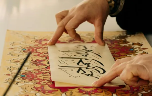 فتاة كتبت عبارة بسم الله الرحمن الرحيم بخط جميل وتضعها فوق لوحة رسمتها بألوان جميلة 