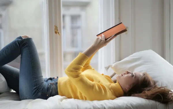 فتاة تقرأ كتاباً وهي مستلقية على السرير 