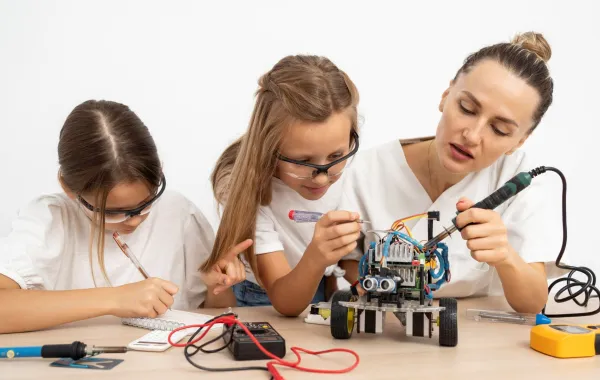 معلمة تساعد طالبتين في بحثهما العلمي