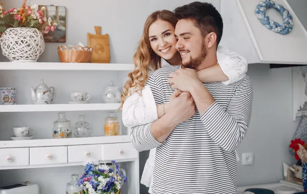 زوجة تحتضن ظهر زوجها وهو يمسك يديها وهما يبتسمان 