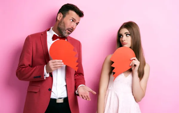 زوجة تمسك نصف قلب مكسور وزوج يمسك النصف الآخر علامة على انكسار العلاقة بسبب الندية 