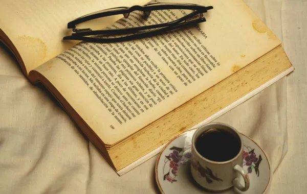 فنجان من القهوة وبجانبه كتاب عليه نظارة