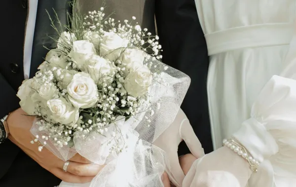 زوج يمسك بيد زوجته في حفل الزفاف ويمسك بيده الأخرى باقة زهور الفرح