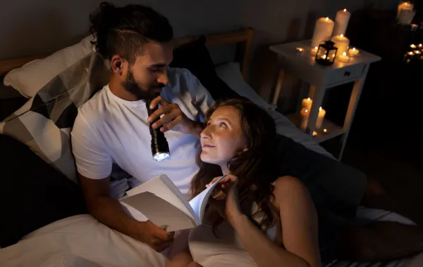 زوج يقرأ مع زوجته بعض الرسائل بالمساء على ضوء كاشف تجمعهما الرومانسية