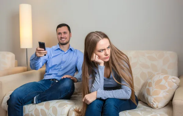 زوج يستمتع بوقته في مشاهدة التلفزيون والزوجة تبدو متضايقة من انشغال زوجها   
