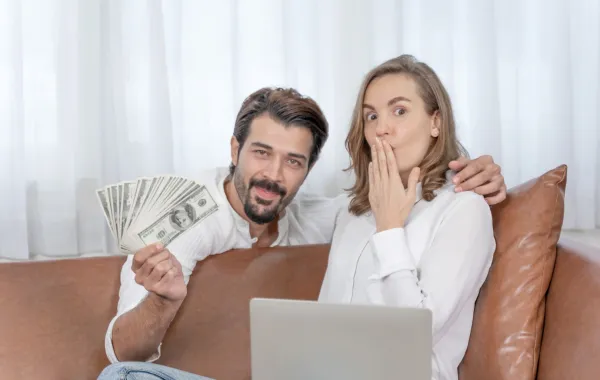 زوج يعطي زوجته مبلغاً من المال وهي سعيدة تجلس خلف اللاب توب  