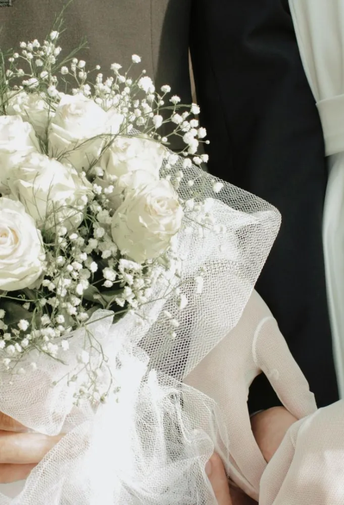 زوج يمسك بيد زوجته في حفل الزفاف ويمسك بيده الأخرى باقة زهور الفرح