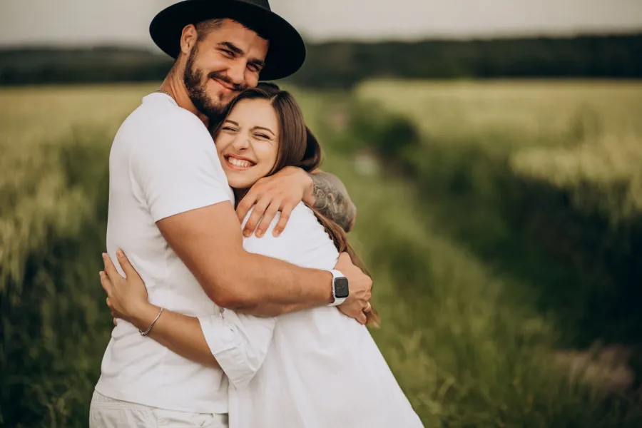 زوج يحتضن زوجته بحنان ومحبة وهي تبتسم بسعادة بين أحضان الطبيعة