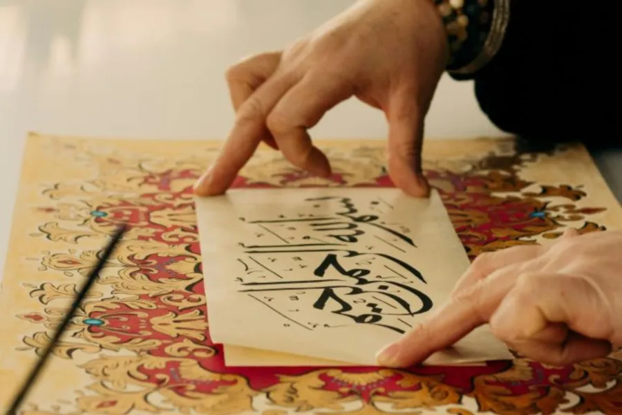 فتاة كتبت عبارة بسم الله الرحمن الرحيم بخط جميل وتضعها فوق لوحة رسمتها بألوان جميلة 